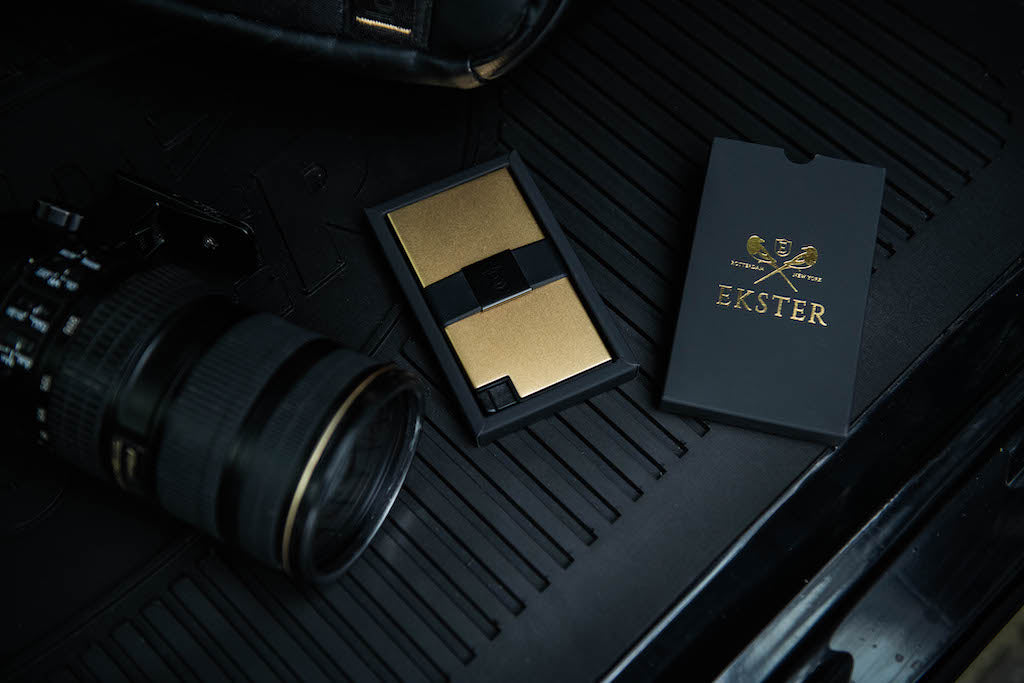 a 18K gold designer card holder wallet lying in between a professional camera and Ekster gift box