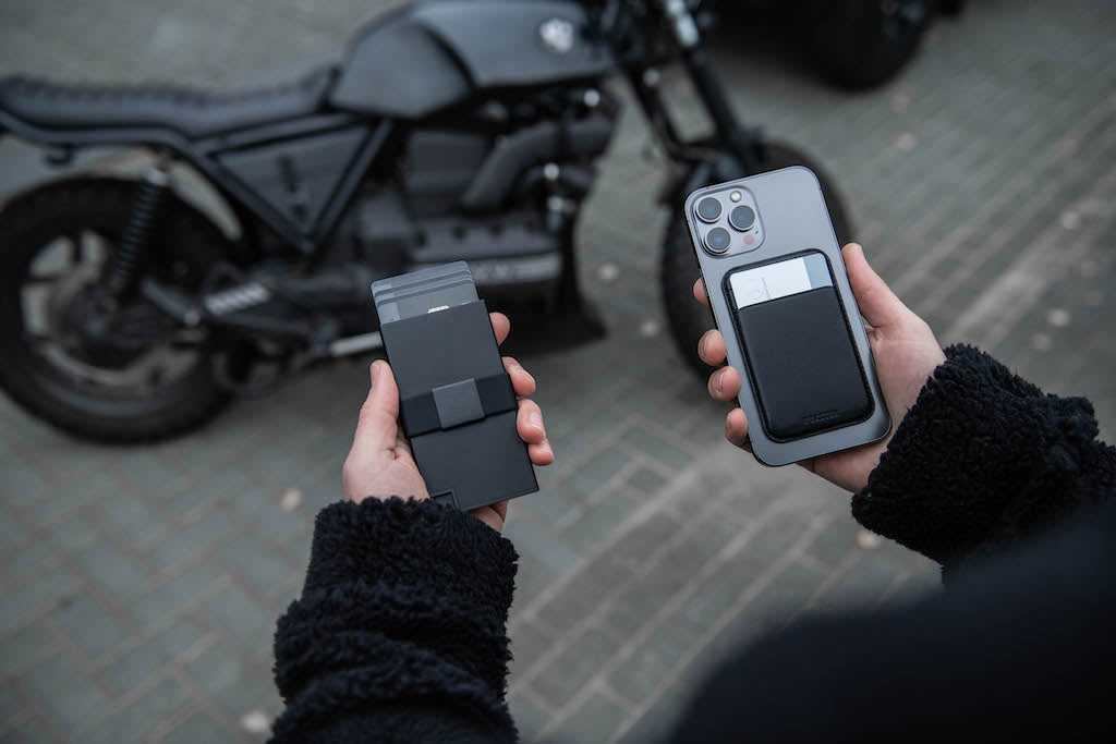 Person’s hands holding iphone with MagSafe cardholder on the back and RFID-blocking black aluminum cardholder in front of jeep