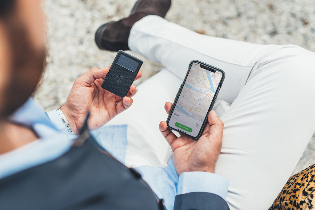 A man holding in his left hand an Ekster wallet tracking device and in his right hand an iPhone screen showing the tracker's location.