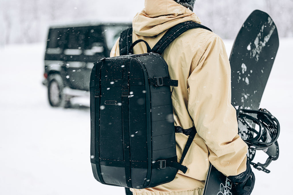 man wearing backpack holding snowboard in the snow