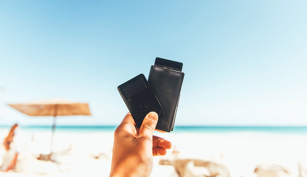 Person holding up the Ekster Wallet Tracker and Parliament Wallet at the beach