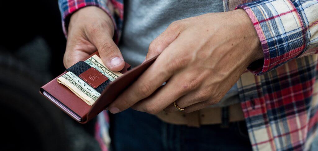 Image of an Ekster smart wallet with a cash strap in a man's hands.
