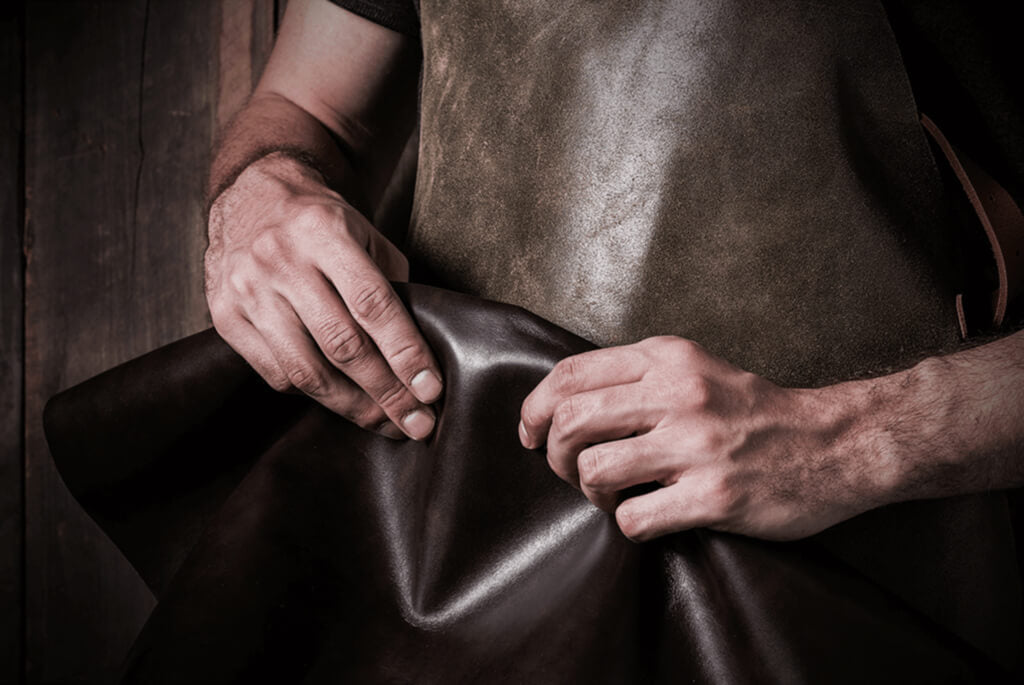 Image of a leather worker's hands, holding uncut leather