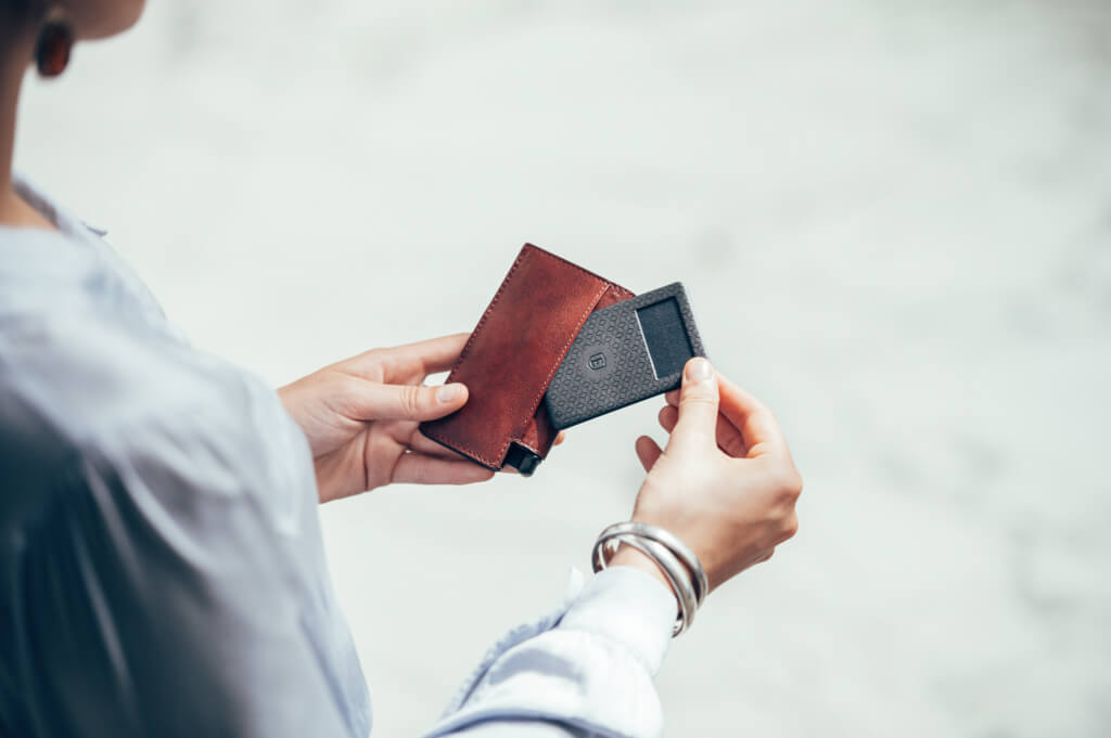 Image of a woman's hands holding an Ekster rfid blocking wallet, with a crowd GPS tracker peeking out from it.