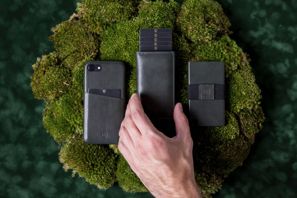 Image of an Ekster iPhone case, and two trendy wallets, side-by-side. A hand reaches for the wallet in the middle, which showcases the card eject function.