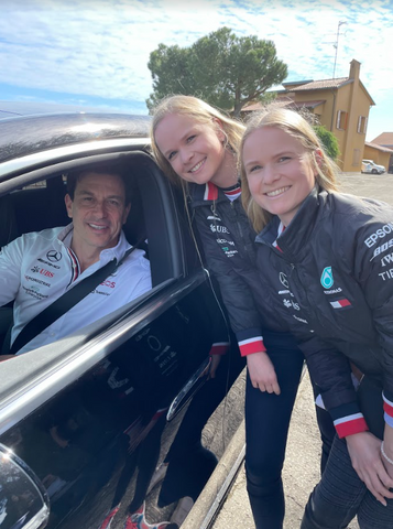Blonde twins greeting Toto Wolff, who is seated in a Mercedes car