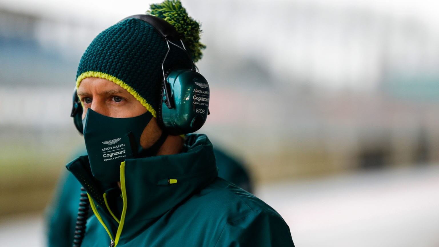 F1 driver Sebastian Vettel in a green coat, hat, and earmuffs.