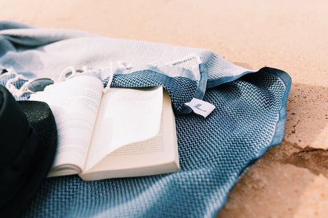 Indigo Luxe Towel next to a book and a sunhat