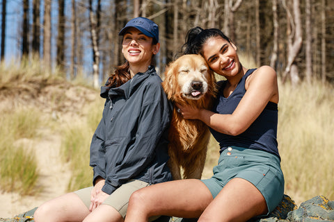 Two women sat with a dog wearing ACAI Summer hiking clothes