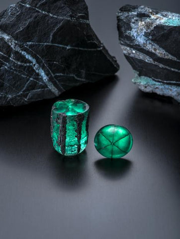 Trapiche emeralds from Penas Blancas mine, Colombia. Rough crystal is 58.83 ct; large cabochon is 22.74 ct. The background consists of two carbonaceous shale rocks with quartz, pyrite and the beginnings of emerald formation. Courtesy of Jose Guillermo Ortiz. Photo by Robert Weldon/GIA.