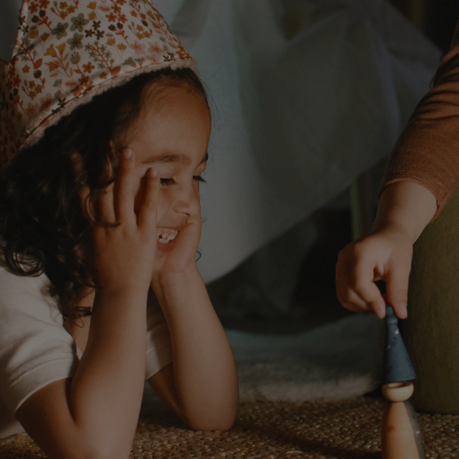 Child playing with a toy on the floor, wearing a floral crown