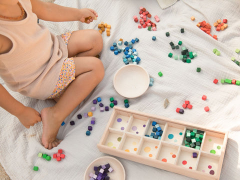 child in shorts and t-shirt sitting on the floor surrounded by grapat wooden loose parts from the mis and match play set