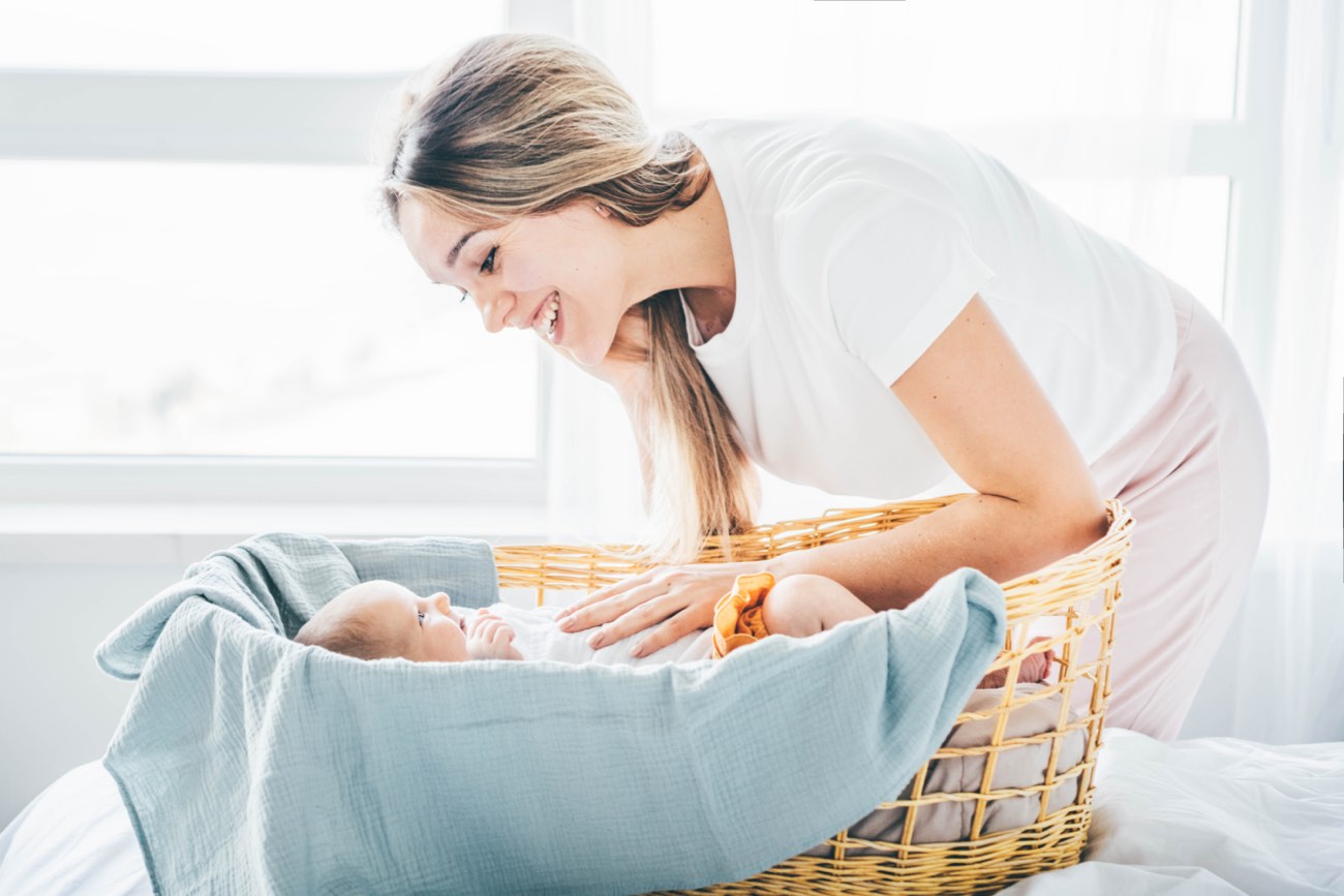 Mother comforts her newborn daughter in her bassinet.