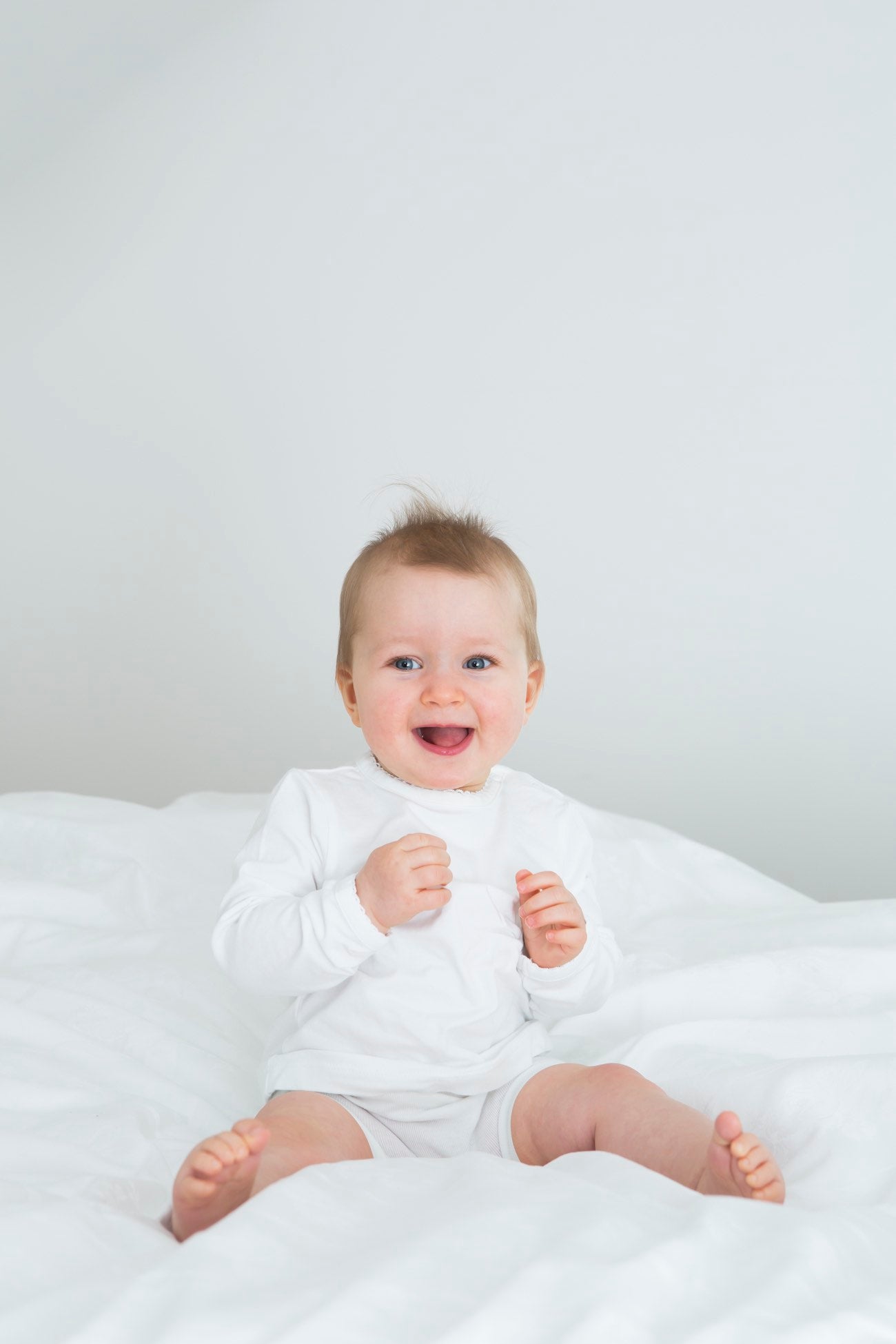 Petite fille souriante assise sur un lit.