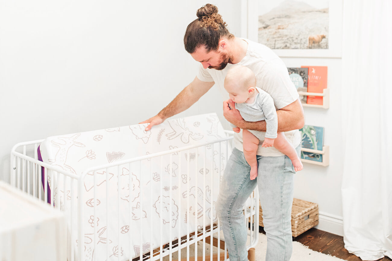Father setting up the Polysleep memory foam baby mattress while also holding his newborn baby.
