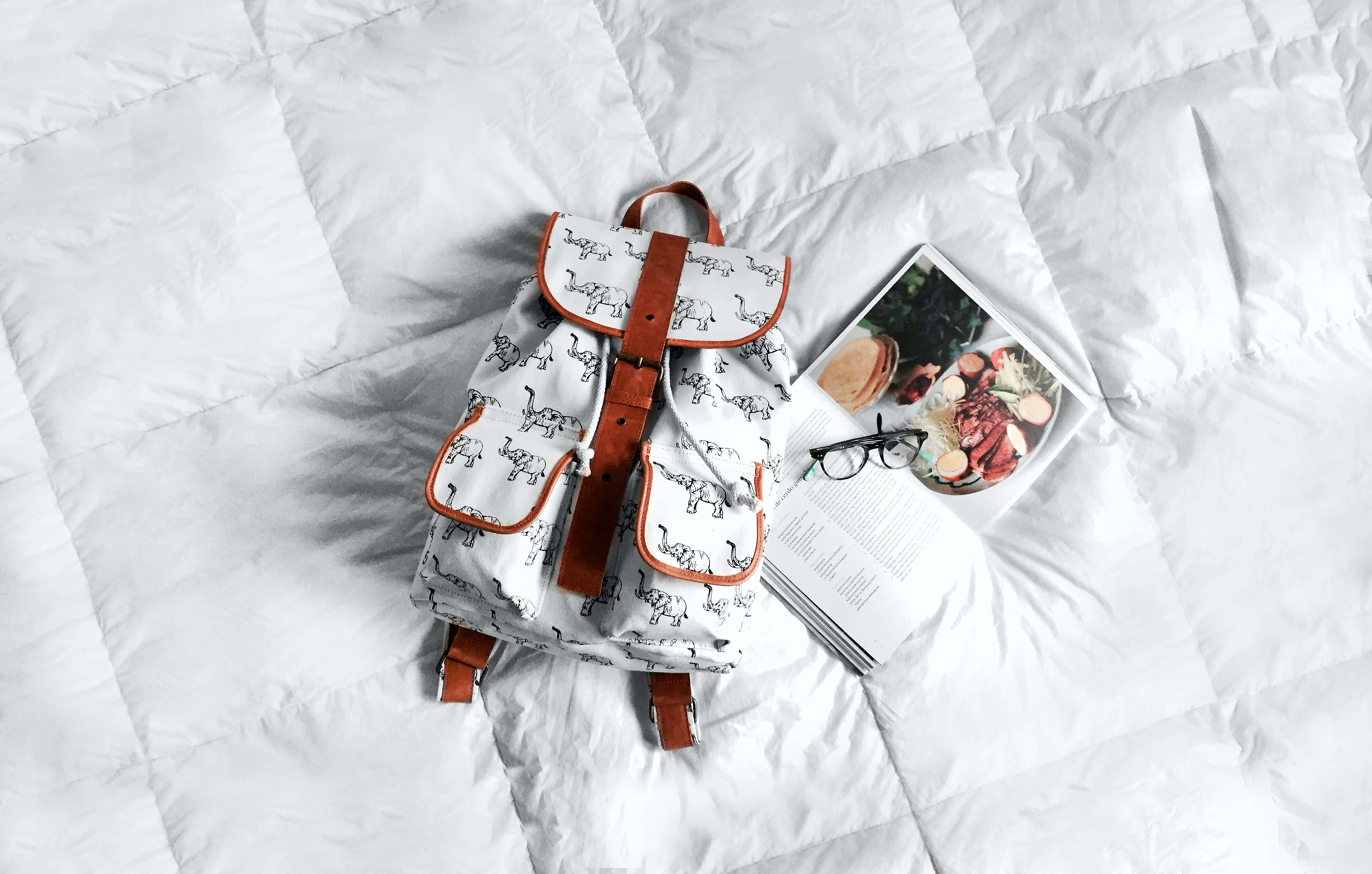 Backpack and school book placed on a duvet bed