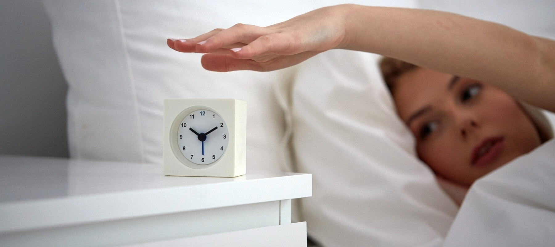 Woman lying in bed, closing her alarm clock on the bedside table