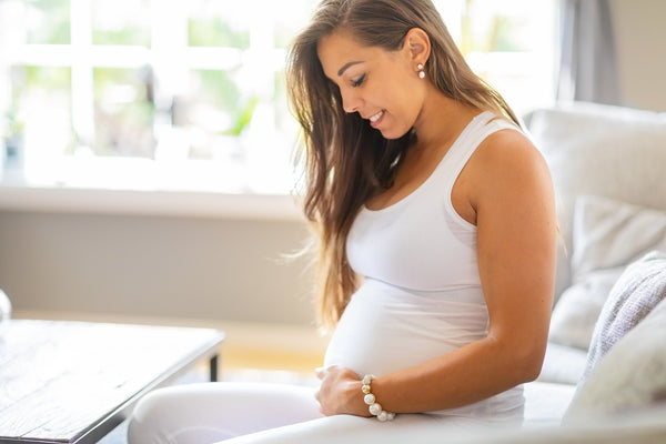 Smiling pregnant woman sitting on the sofa touching her belly