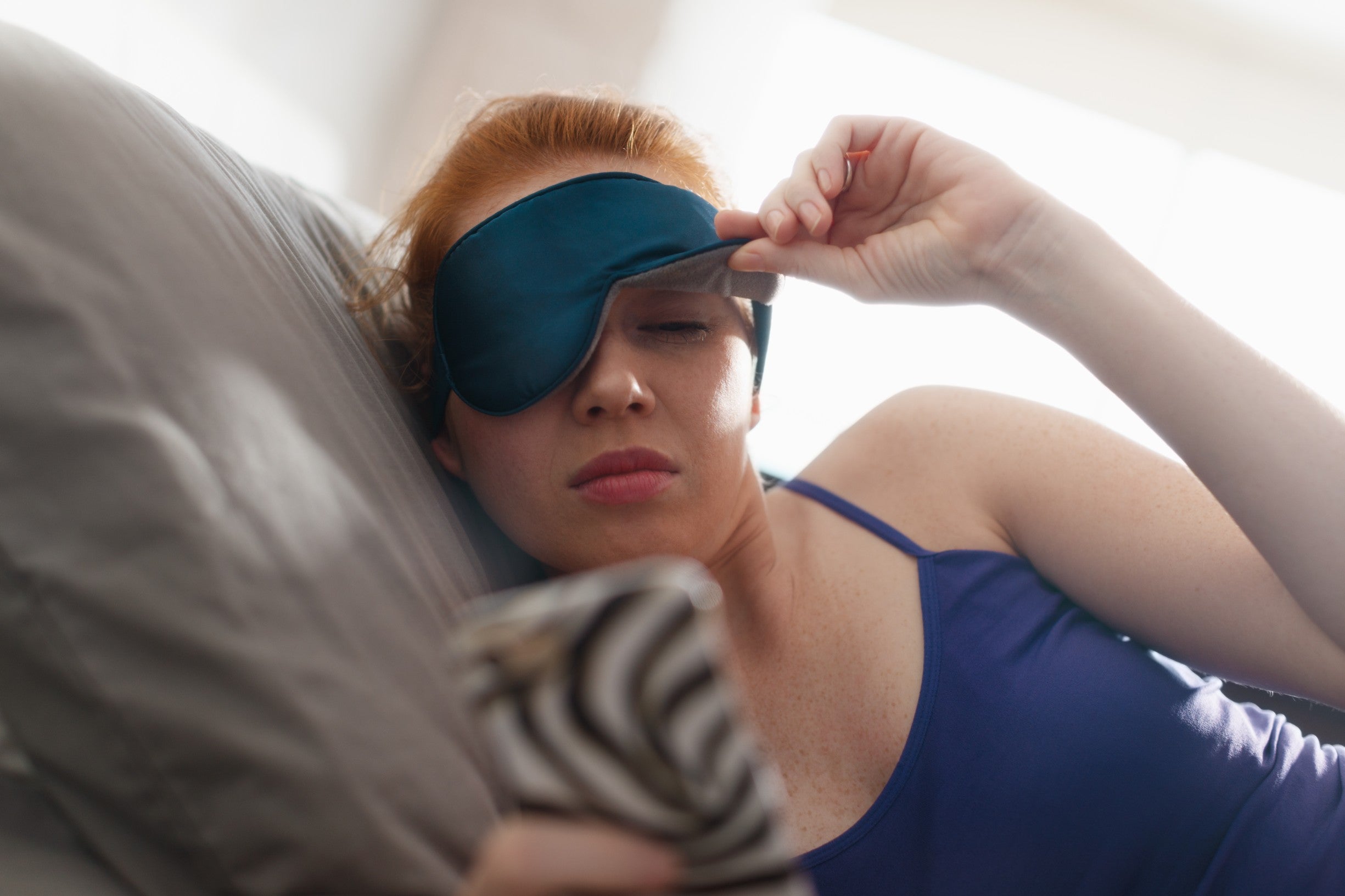 Young woman lifting her eye mask up to look at her phone
