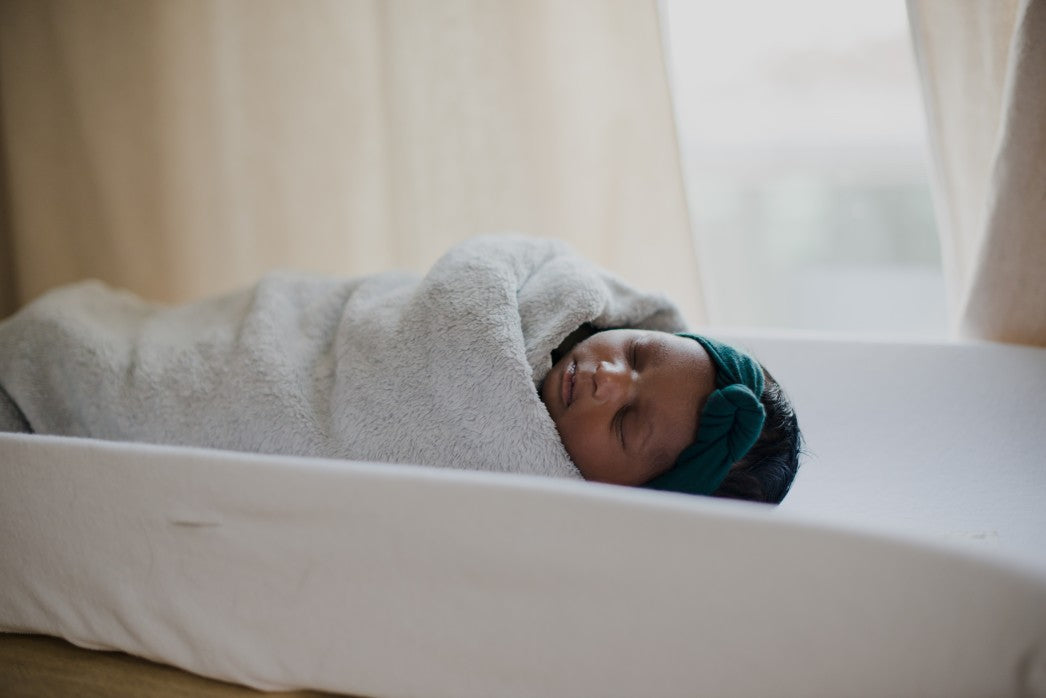 Baby sleeping wrapped in a blanket including a headband on the edge of a window