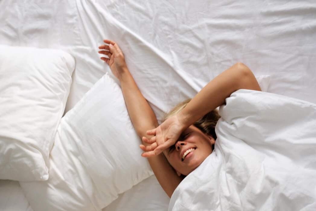 Smiling woman lying in bed with head pointing west