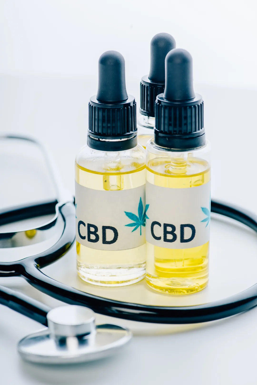 Three containers of CBD oil and stethoscope on a white background.