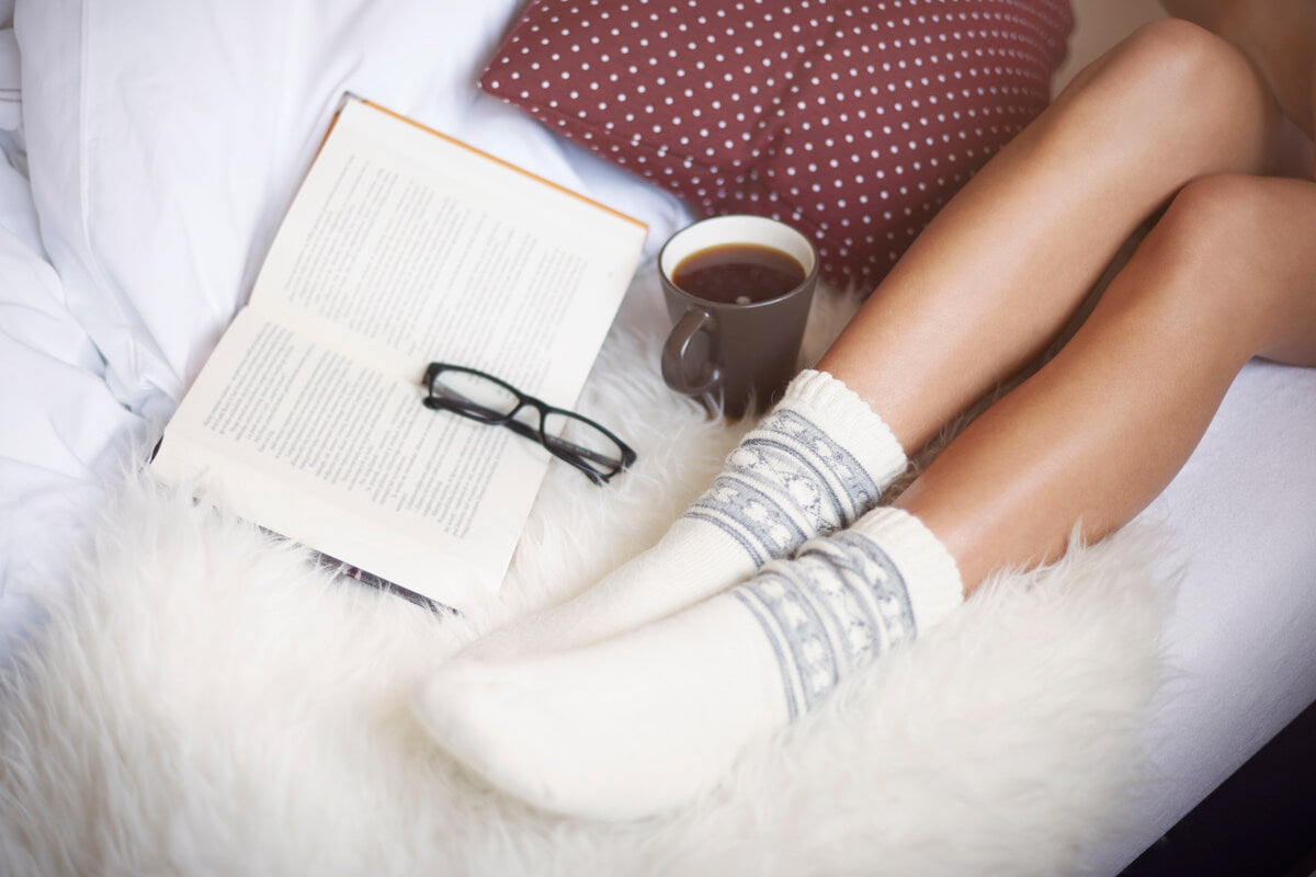 The low-raised legs of a woman on a white foam cushion including her coffee and her book