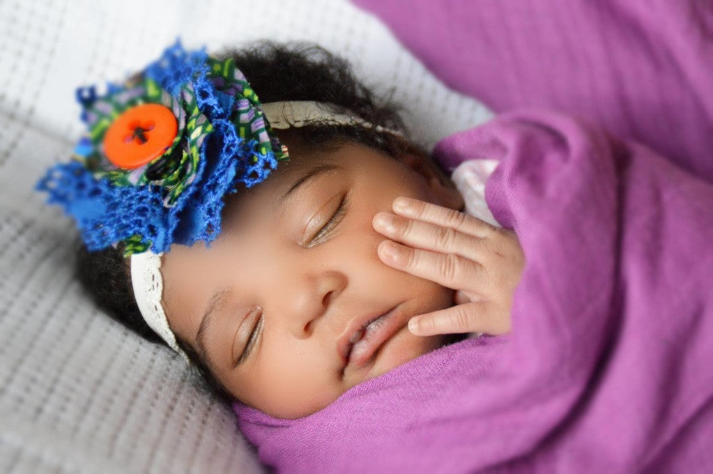 Close-up of a sleeping baby wrapped in a pink blanket with a floral headband around his head