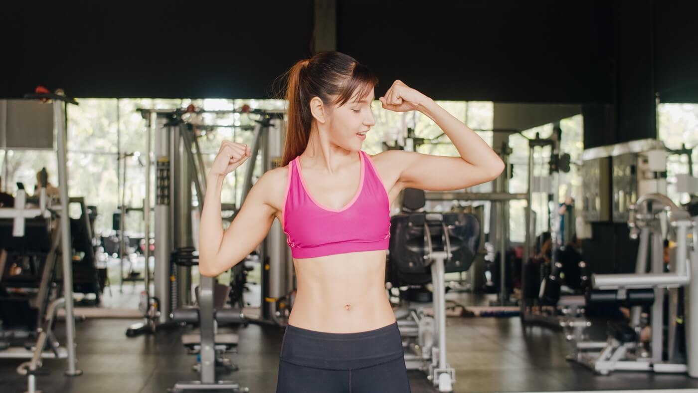 healthy athlete woman with sportswear smiling looking at her arm muscles