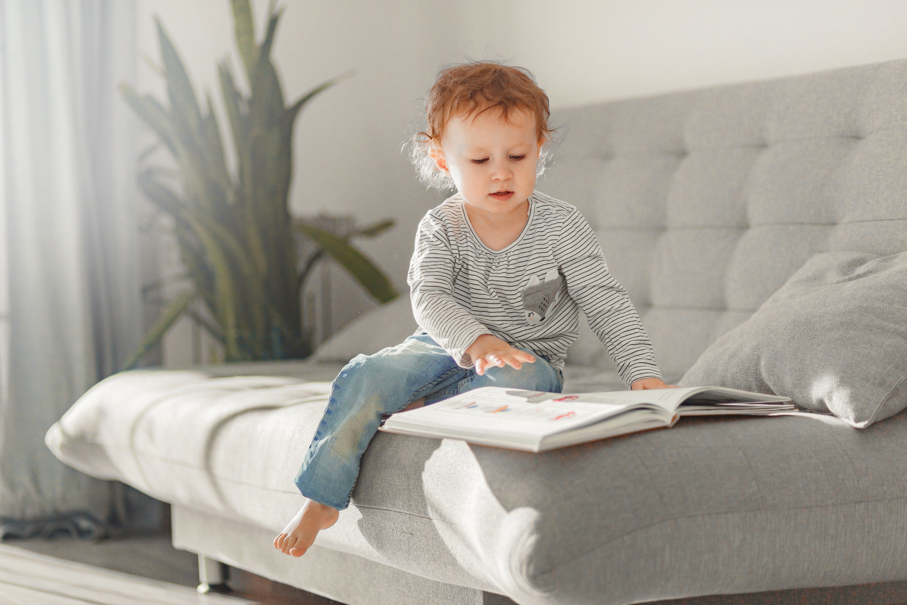 2 year old little girl reading a book on a bed