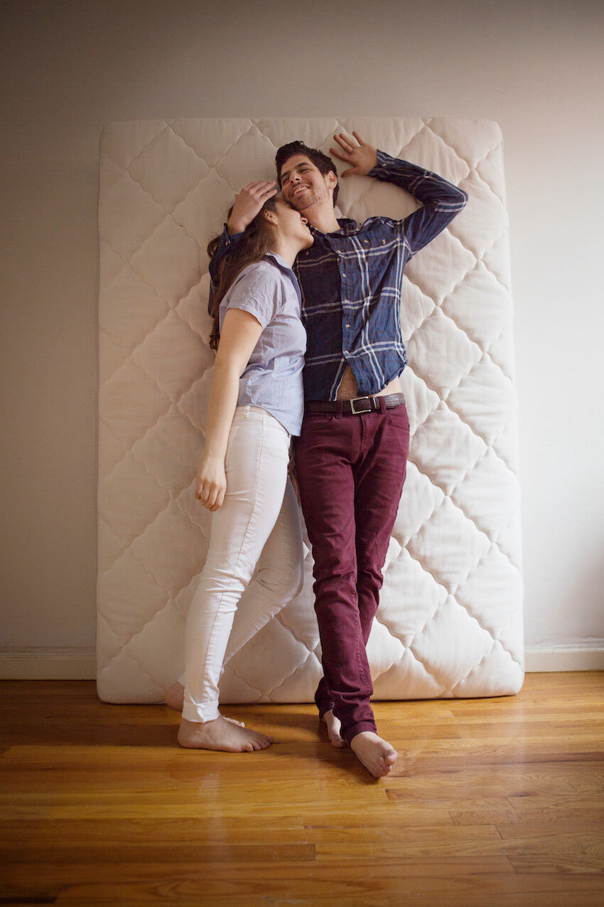 A couple lying on a mattress standing against a wall.