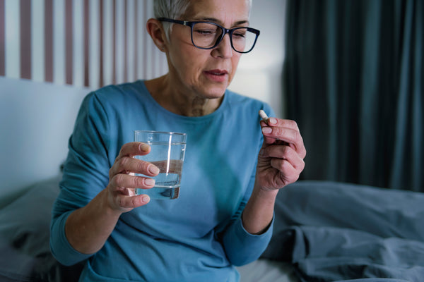 Femme aînée sans sommeil souffrant d'insomnie, tenant un somnifère et un verre d'eau dans les mains