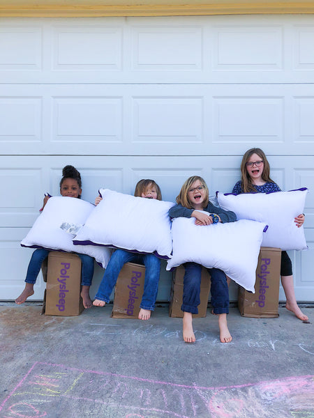 4 petites filles assises sur les boites de livraison tiennent des oreillers Polysleep dans leurs mains
