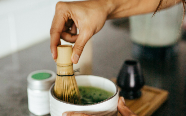 a female hand prepares premium matcha green tea powder by using a bamboo whisk during ceremony