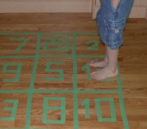 Numbered squares on the floor made of masking tape. A child is standing on one of the squares prepared to jump to the next number.