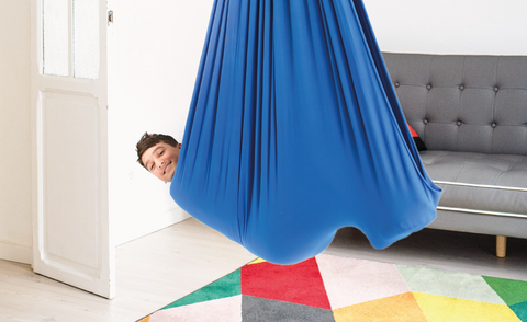 a boy is using a blue sensory swing in a living room