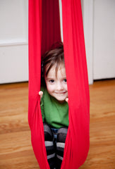 A girl is hiding in a red sensory swing.