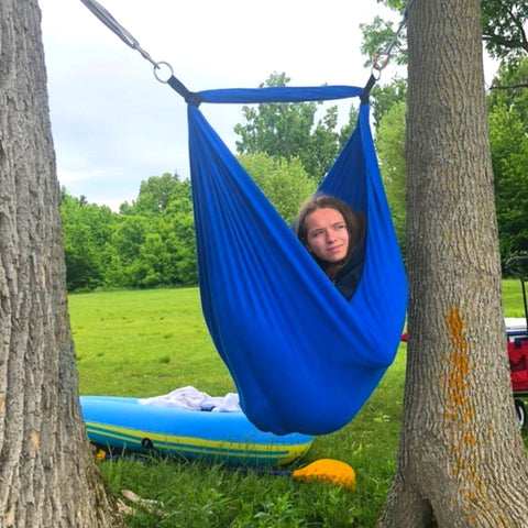 A girl is enjoying a sensory swing installed between two trees.