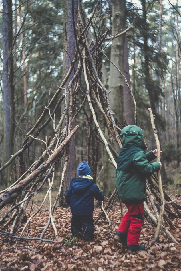 Two children are playing outside playing with sticks building a shelter.