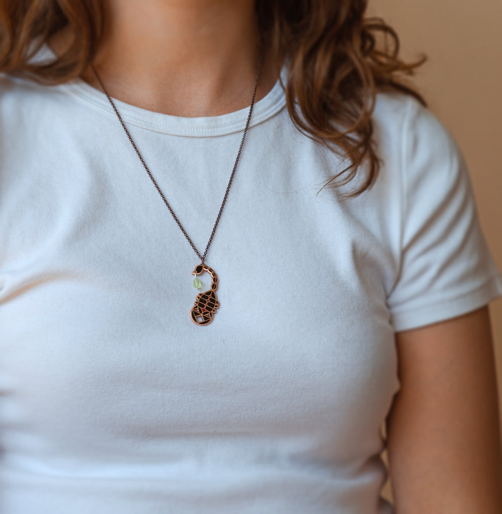 A person wearing an Ishara scorpion black enamel necklace. Shows where it sits just below the collarbone.