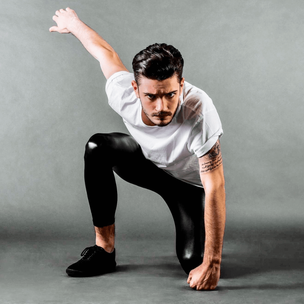 man croushing in superhero pose wearing shiny metallic black leggings