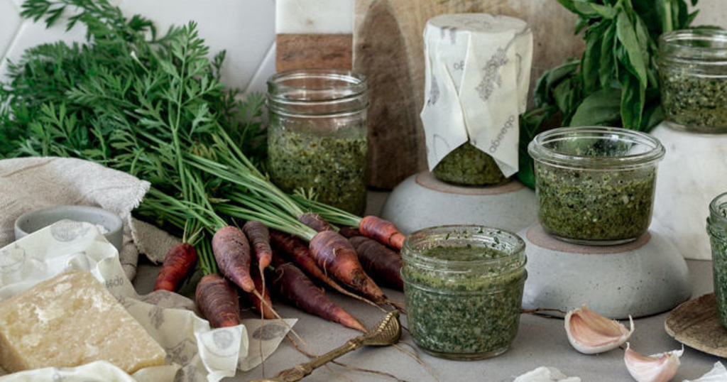 carrots, parmesan, and jars of carrot top pesto covered with Abeego food wrap