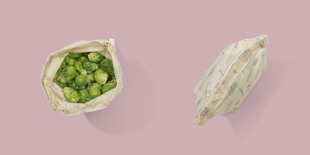 Abeego bag full of Brussels sprouts opened next to a closed Abeego bag. Pink background.