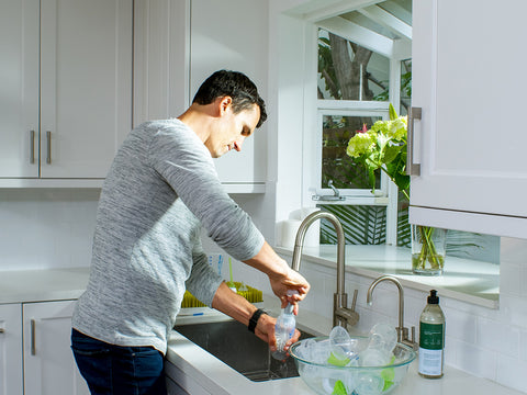 man washing bottles using a bottle brush inside a kitchen at the sink