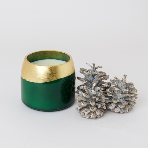 Firefly Aglow Tree Farm scented candle with green candle vessel and gold accents next to 3 pine cones on white background