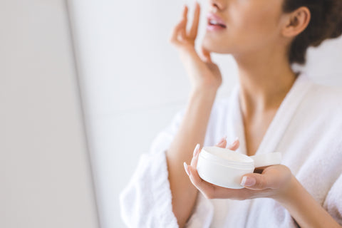 Mujer aplicando crema facial mientras usa una bata de baño de felpa blanca