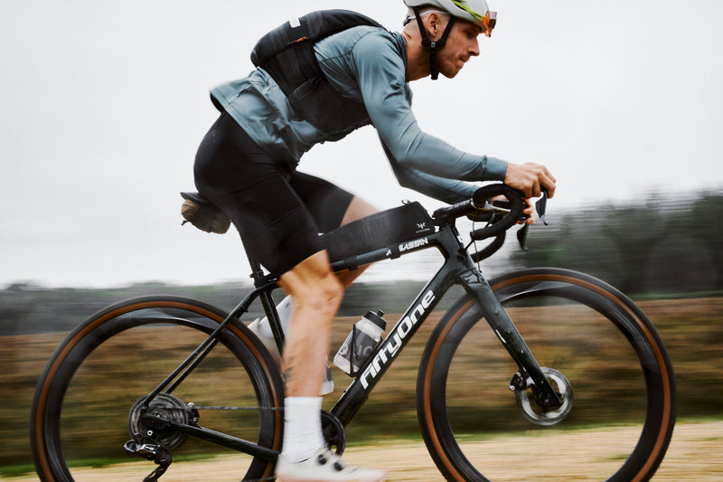 Man riding a bike wearing a blue top, black vest and black cycling shorts