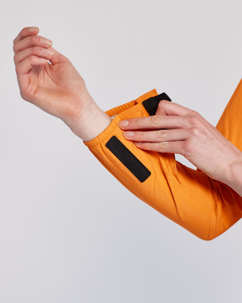 Close up of a person holding the velcro on the sleeve of an orange rain jacket