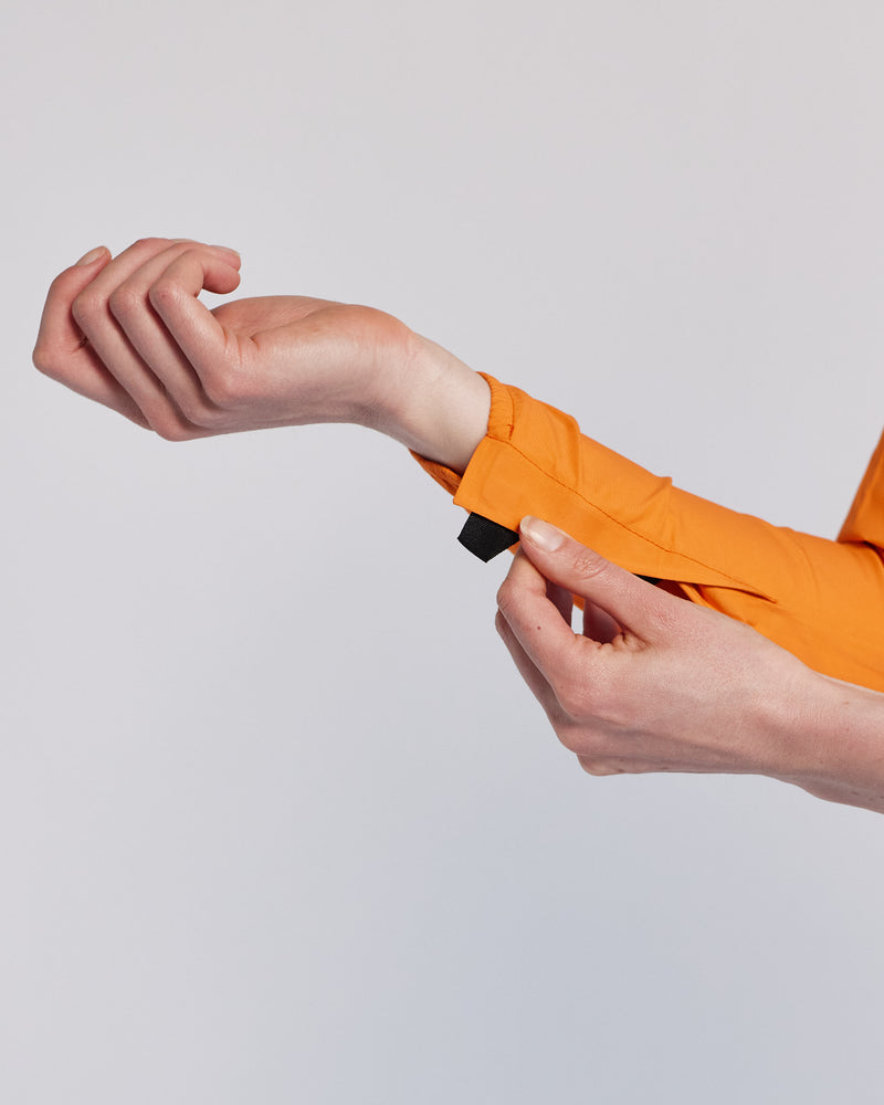 Close up of a person folding the velcro sleeve of an orange rain jacket