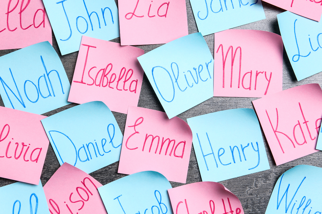 GPT Assorted sticky notes in pink and blue are scattered across a gray surface, each note featuring a different name written in various hues of blue and pink markers.